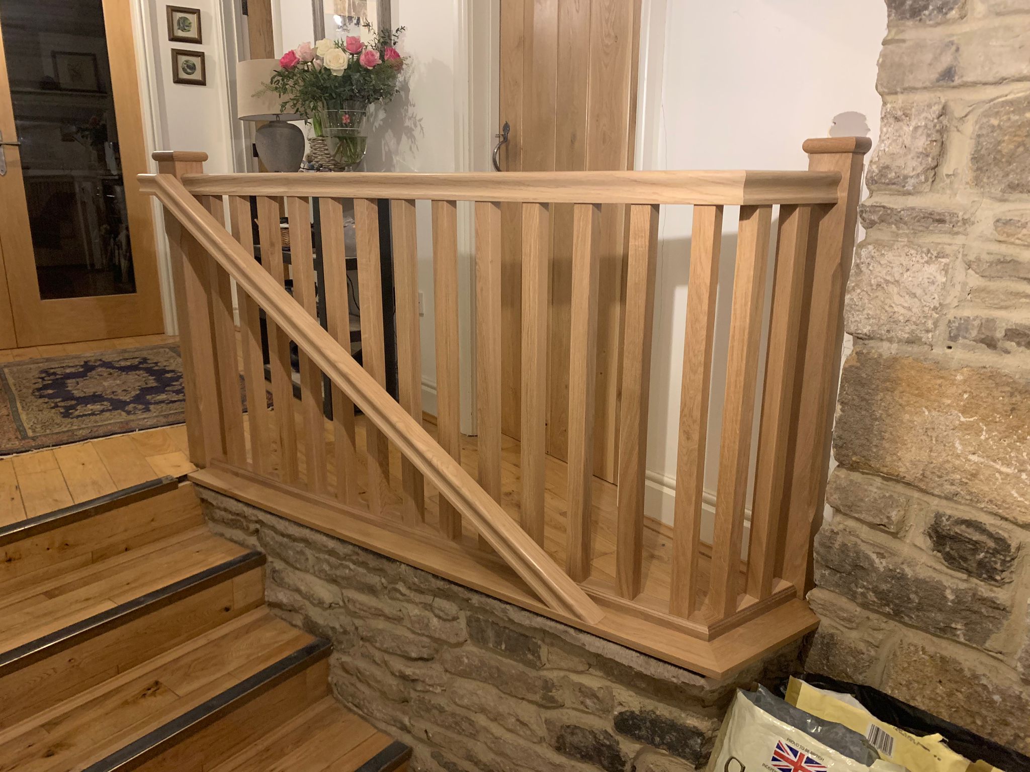 An oak staircase and balustrade beside a stone wall